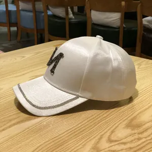 Close-up of white satin baseball cap featuring black rhinestone N logo on wooden table
