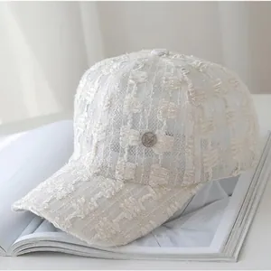 Close-up of white lace baseball cap featuring textured mesh and silver metal badge