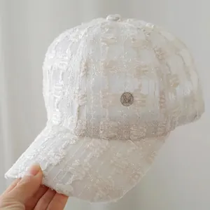 Close-up of white lace baseball cap with intricate mesh texture and silver M logo