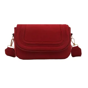 Red faux suede saddle crossbody bag with quilted flap and gold hardware on white background