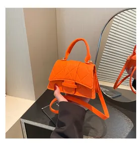 Detail of a bright orange mini square bag featuring classic quilted stitching and handle