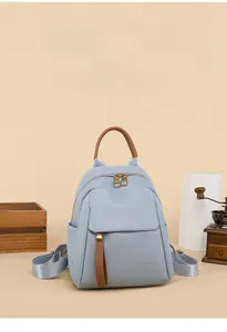 Detail of light blue Oxford backpack featuring brown leather handles and dual zippers
