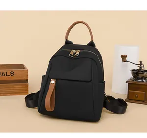 Detail view of the black mini oxford backpack with brown leather handle and gold metal zippers