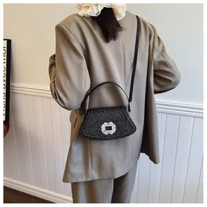 Détail du sac à bandoulière noir à paillettes avec boucle strass porté sur un blazer kaki
