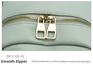 Detail view of smooth double-way gold metal zippers on a green oxford fabric backpack