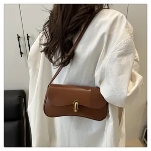 Detail of a brown leather shoulder bag with a gold metal clasp shown on a white shirt