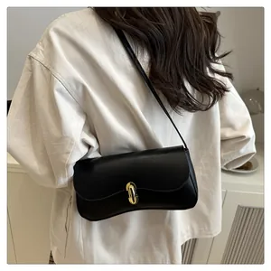 Close-up of minimalist black shoulder bag with gold oval twist lock on a neutral model