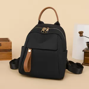 Chic black Oxford cloth backpack with brown leather handles on a minimalist display stand