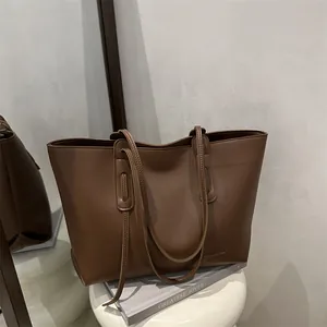 Grande borsa tote in pelle marrone scuro con manici sottili ed etichetta moda su sedia bianca