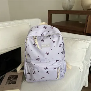 Sac à dos d'école lavande avec motifs nœuds mauves et étiquette FASHION sur canapé blanc
