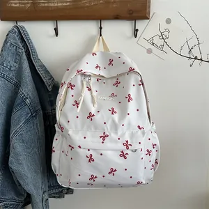 Sac à dos d'école blanc avec nœuds rouges et poche avant dans un décor de style campus