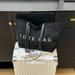 Large black suede tote bag with TOTE LAG print on white suitcase for travel