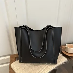 Minimalist large black tote bag with shoulder straps for women in a cozy interior setting