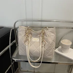 Quilted off-white large tote bag with chain strap on a minimalist metal shelf
