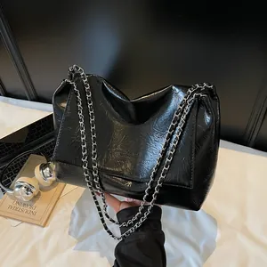 Fashionable black glossy wrinkled leather tote bag with silver chain strap shown in lifestyle