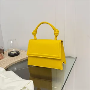 Minimalist yellow structured trapezoid handbag with decorative knot handle and flap closure