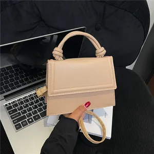 Minimalist beige crossbody box bag with knot handle detail and gold hardware accents