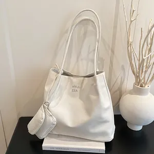 Minimalist beige tote bag with shoulder straps and small zipper pouch on a book