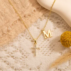 Detail der Goldkette mit Zirkon-Kreuzanhänger und Buchstabe M auf warmem Stoffhintergrund