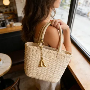 Dettaglio di una borsa tote in paglia intrecciata con un ciondolo a lettera A dorata