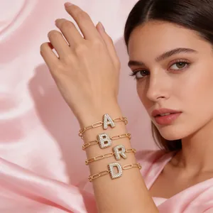 Gouden armbanden met kristallen ballonletters A, B, R, D op roze zijden achtergrond
