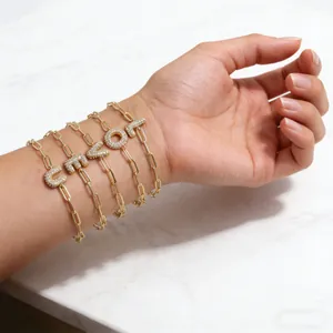 Detail van vijf gouden paperclip armbanden met sprankelende zirkonia letter hangers
