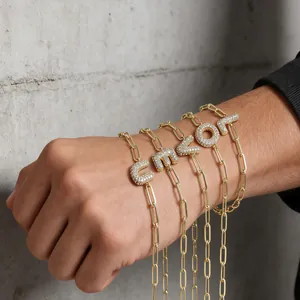 Detailopname van gouden paperclip armbanden met pavé gezette zirkoon letterhangers