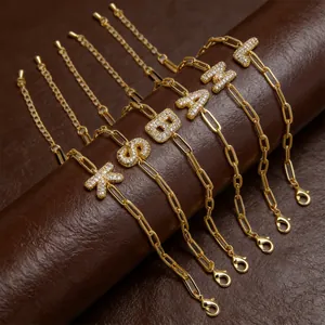 Detail van gouden paperclip kettingarmbanden met zirkonia letterbedels op een rol