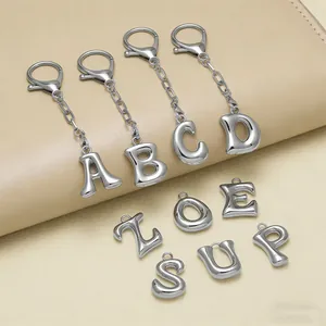 Ciondoli alfabeto in metallo argento lucido con moschettoni su sfondo in pelle beige