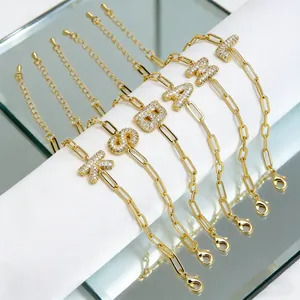 Detail van gouden paperclip-kettingarmband met zirkonia geplaveide letterhangers