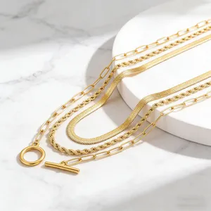 Close-up of golden layered necklaces set with OT buckle, rope chain and snake chain details