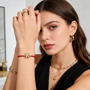Detail eines roten geflochtenen Armbands mit vergoldetem, kristallbesetztem K-Anhänger