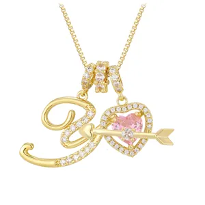 Detail of gold necklace with pink heart gem, arrow pendant and cursive letter