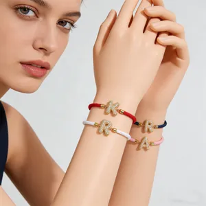 Makroaufnahme bunter geflochtener Seilarmbänder mit vergoldeten Buchstabenanhängern