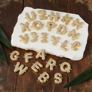Nahaufnahme von vergoldeten Kupfer-Alphabet-Anhängern mit Zirkon auf Marmorhintergrund