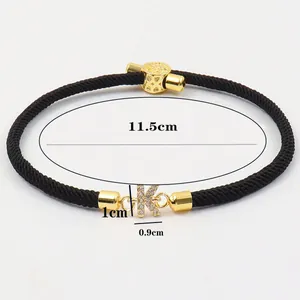 Detail eines schwarzen geflochtenen Armbands mit goldenem Buchstaben K Anhänger und Zirkonia
