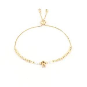 Detail eines goldenen Perlenarmbands mit Perlenakzenten und personalisiertem R-Anhänger