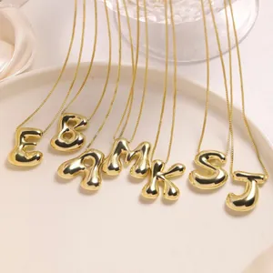 Glanzende 18K vergulde bubble letter kettingen A-Z op een wit keramisch plateau