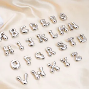 Makroaufnahme von silbernen 3D-Ballon-Buchstabenanhängern auf champagnerfarbener Seide