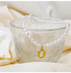 Detail einer weißen Perlenkette mit goldenem Buchstaben-O-Anhänger am Milchglas