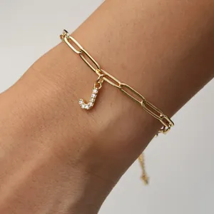 Detail of letter J pendant paved with zircons on gold paperclip chain bracelet