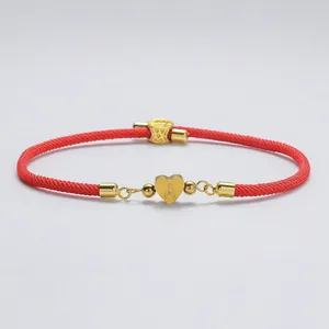 Detail eines roten geflochtenen Armbands mit goldenem Herzanhänger und Gravur Buchstabe A