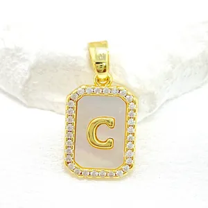 Détail d'un pendentif en nacre dorée avec bordure en zircone et lettre C gravée