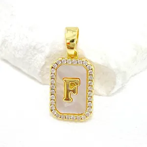 Détail d'un pendentif carré doré en nacre avec la lettre F et incrustation de zircon
