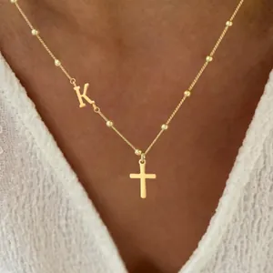 Minimalist gold necklace featuring letter K and cross pendant on a beaded fine chain