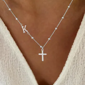Minimalist beaded chain necklace featuring a silver cross and initial letter K pendant
