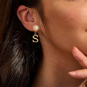 Detailaufnahme einer Perlenohrring mit poliertem goldenem S-Anhänger an einem Model