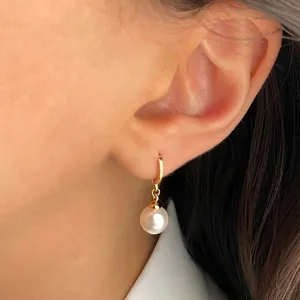 Close-up of elegant gold hoop earrings with white round pearls worn by a female model