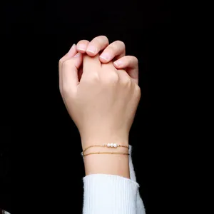 Bracelet élégant à double chaîne dorée orné de trois perles blanches sur fond noir