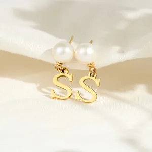 Detailaufnahme von Perlenohrringen mit goldenem Buchstaben 'S' auf weißem Stoff